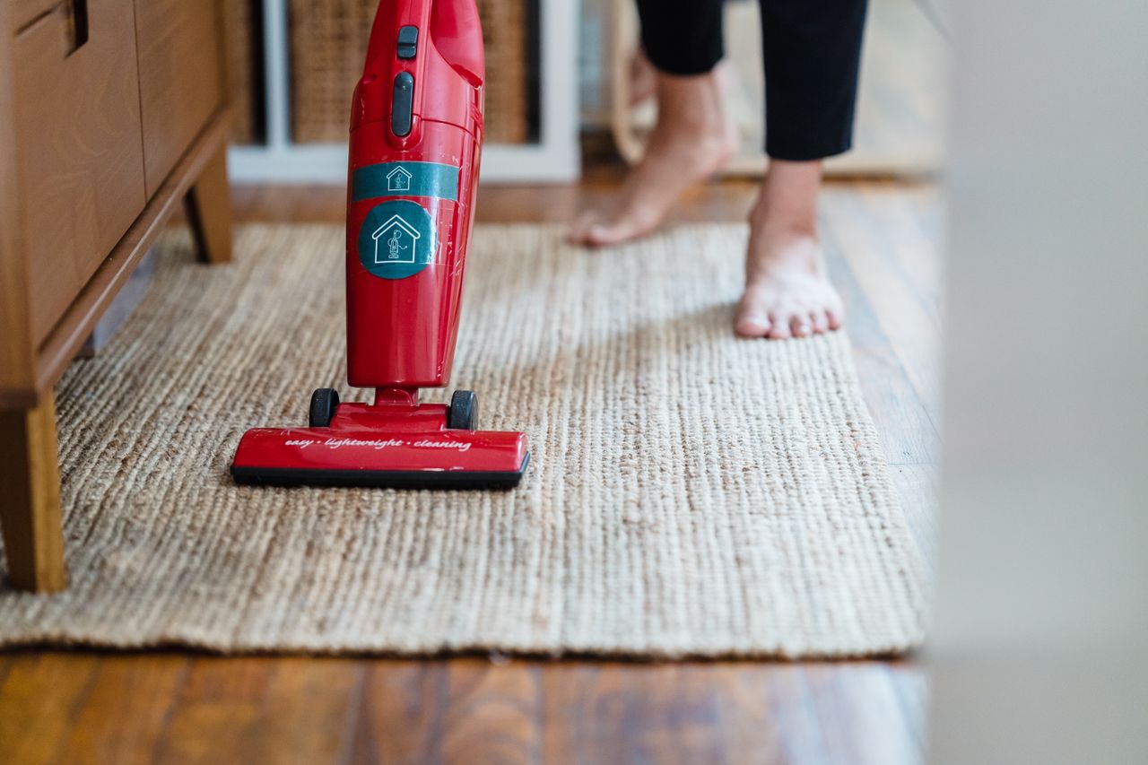 A red vacuum cleaner sits on a carpet in a stylish home setting, with the user barefoot.